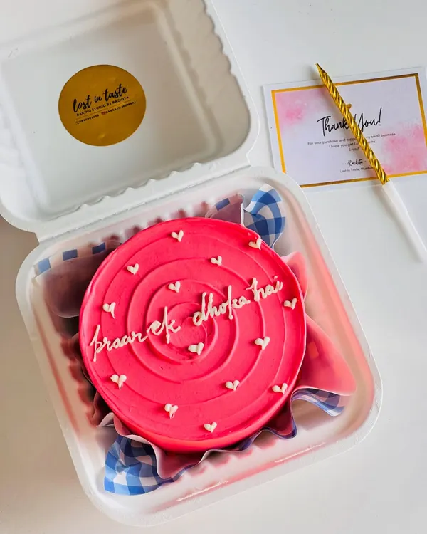 A fun and quirky bento cake with a bright pink swirl design and the message "pyaar ek dhoka hai". It's perfect for a laugh with a friend.