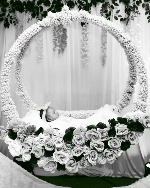 A serene black and white photo of a newborn resting in a magnificent circular cradle adorned with white flowers. This shot highlights the beauty and artistry of the event's decor.