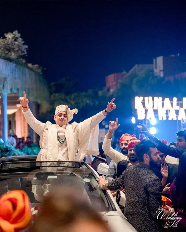 A groom making a rockstar entrance for his baraat, standing on top of a car, ready to celebrate.