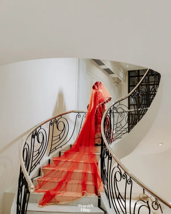 A bride's descent down a spiral staircase, her magnificent red veil trailing behind her. This is a portrait of pure drama and elegance, a fairytale moment brought to life.