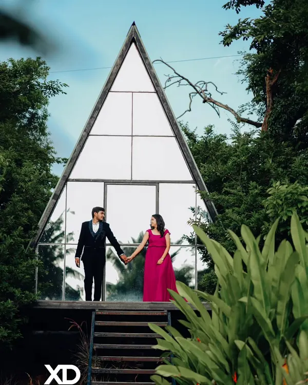 Holding hands before their new beginning. This shot at a Bangalore studio highlights the couple against the modern glass structure, with the lush greenery framing them perfectly. It's a classic romantic pose with a contemporary feel.