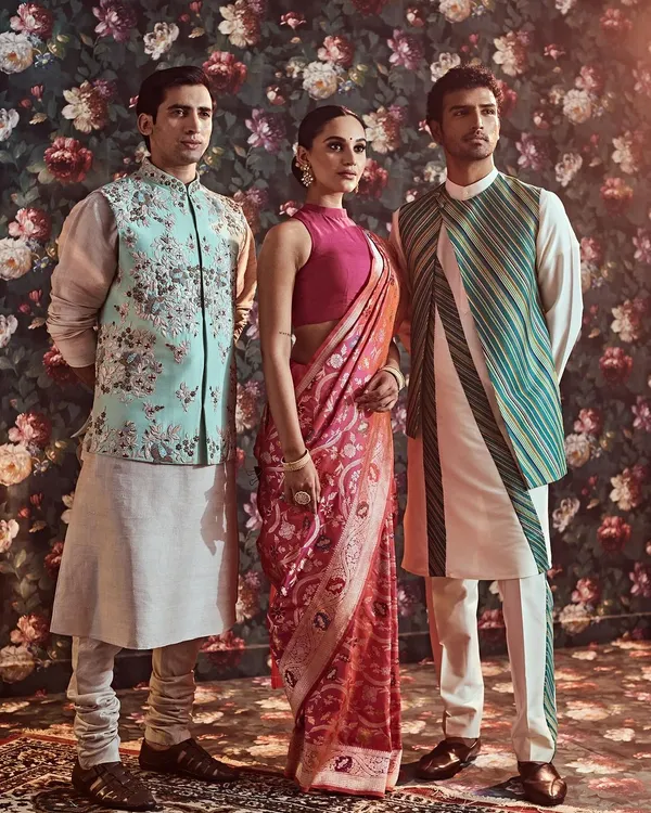 A portrait of coordinated elegance. This look features a vibrant pink Banarasi silk saree paired with a pastel blue floral embroidered jacket for him, showcasing our ability to create harmonious ensembles for couples and families.