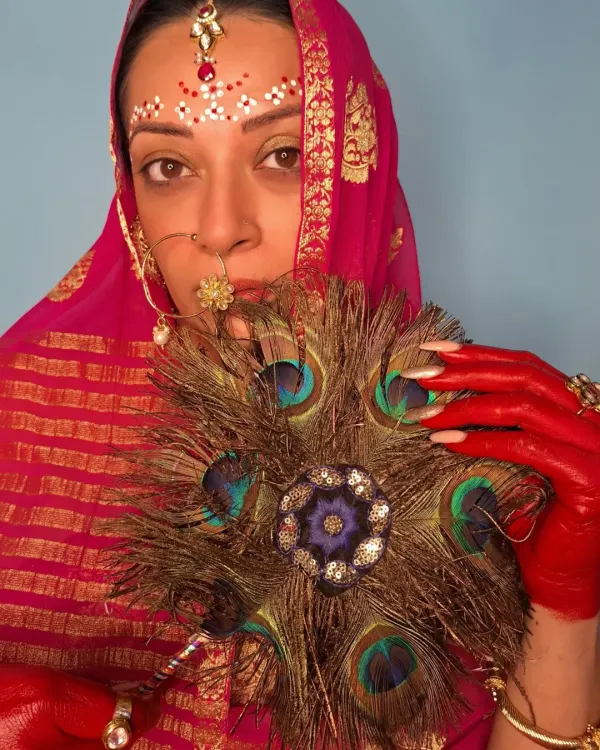 A conceptual look inspired by Radha for Janmashtami. The styling involves traditional elements like a pink bandhani dupatta, a maang tikka, and a nath, but with an artistic twist: the hands are painted with red alta, and the forehead has intricate bindi art.