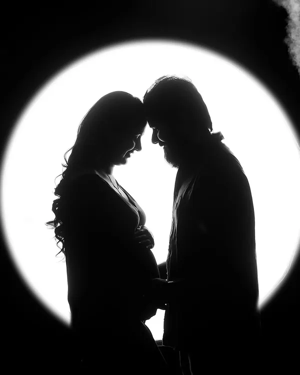 A stunning maternity silhouette of a couple against a circular light source. This artistic black and white photo creates a feeling of intimacy and wonder.