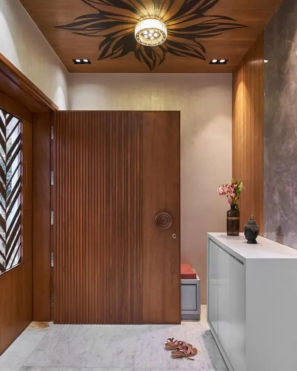 We designed this stunning entryway to make a memorable first impression. A fluted wooden main door is complemented by a side panel with a geometric cutout, and the ceiling features a beautiful floral art detail.