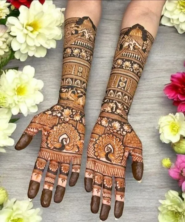 This beautifully staged photo shows a classic Rajasthani design with symmetrical peacocks on the palms and intricate architectural details on the arms, surrounded by fresh flowers.