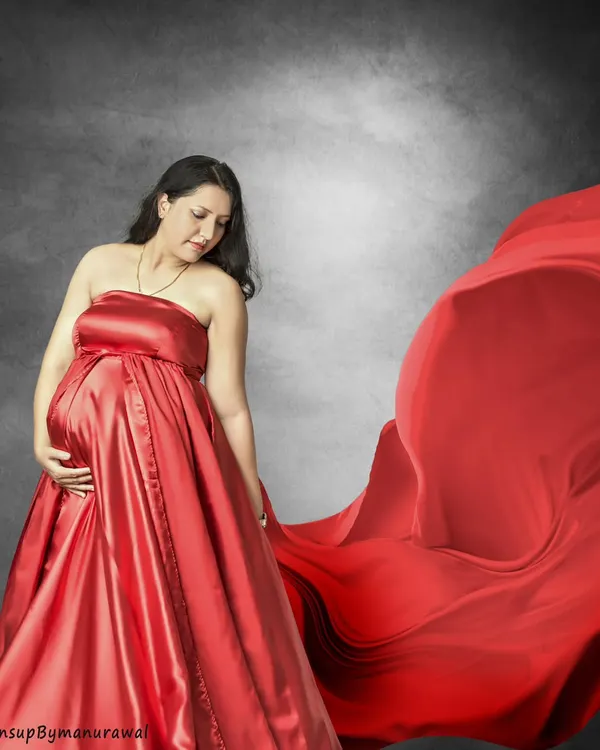 The power of a classic red gown. This studio portrait uses dramatic fabric and soft lighting to create a timeless and elegant image, focusing on the mother's serene expression as she holds her baby bump.