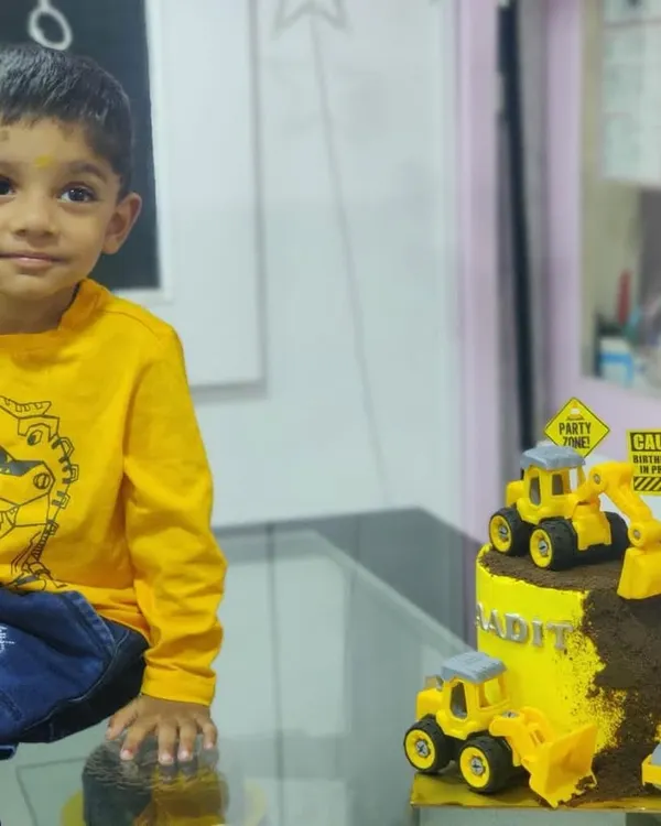 A young birthday boy sitting proudly next to his custom-made construction theme cake.