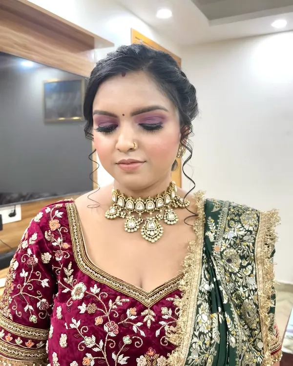 A close-up of a classic bridal look featuring a dramatic purple smokey eye and a neutral lip, perfectly complementing the rich velvet lehenga. The skin is kept radiant to catch the light beautifully.