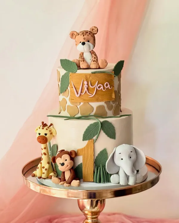 This two-tiered jungle safari cake is perfect for a first birthday. It features a giraffe-print top tier and fondant figures of a leopard, giraffe, monkey, and elephant.