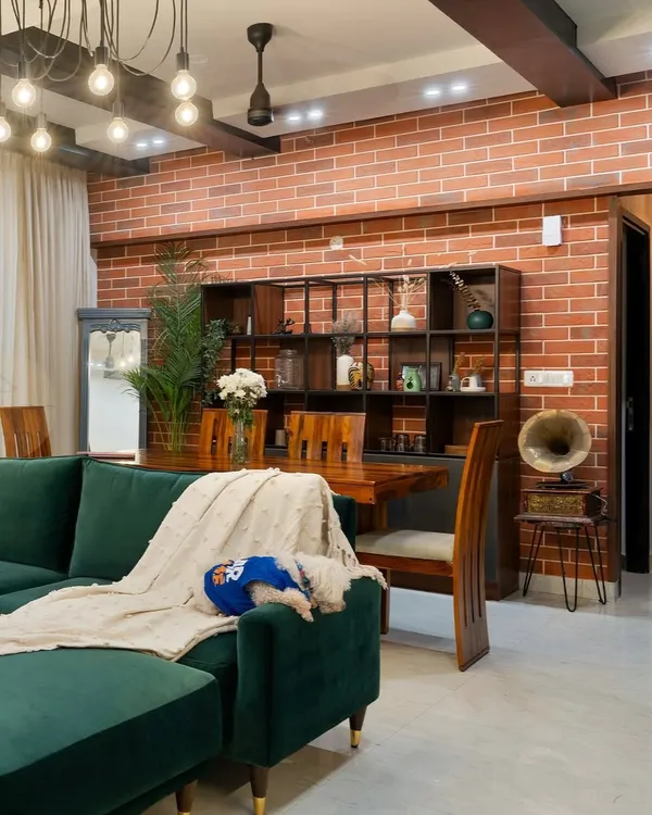This industrial-chic living room features a raw brick accent wall, a deep emerald green sofa, and custom wood shelving. The space is a perfect mix of refined and rustic, with our puppy Cookie adding a touch of homeliness.