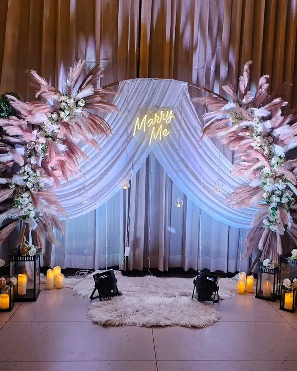 A dreamy marriage proposal setting with a 'Marry Me' neon sign, elegant pampas grass arrangements, and the warm glow of candles. We create unforgettable moments for you to pop the question in style.