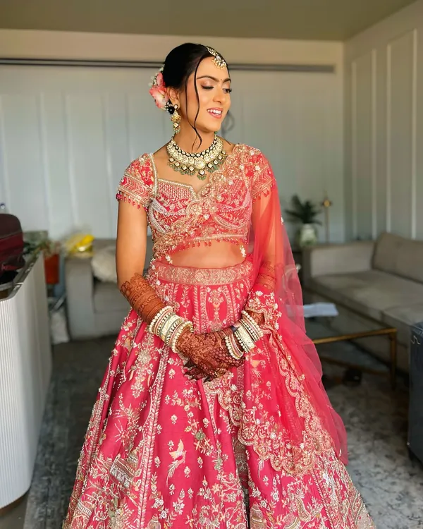 A beautiful bridal updo for a day wedding. I created a neat bun and adorned it with fresh pink flowers to match her lehenga.