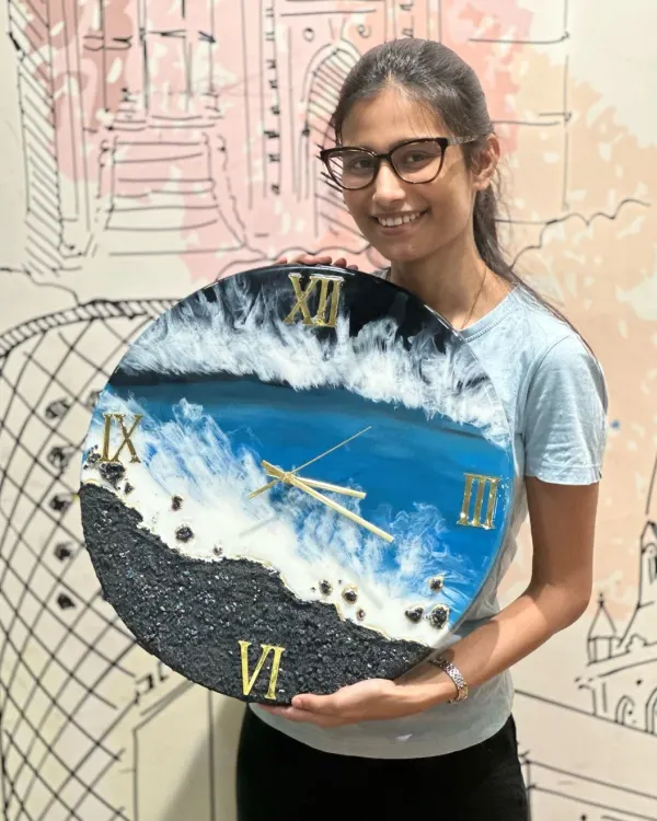 A student proudly holds up the gorgeous ocean-themed resin clock she created, complete with realistic waves and a textured sand effect.