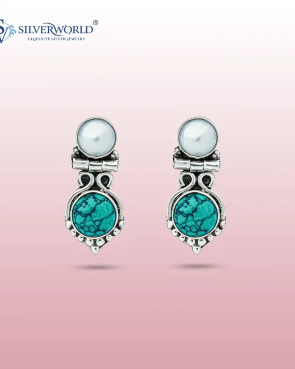 These elegant earrings feature a vibrant turquoise stone set in an oxidized silver frame, topped with a luminous white pearl. The design combines color and classic elements for a sophisticated look.