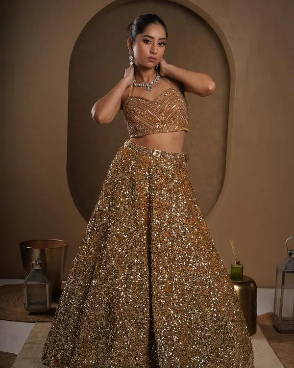 A full-body shot where the model looks directly at the camera, creating a powerful connection with the viewer. The lighting is set to make every sequin on the golden lehenga sparkle.