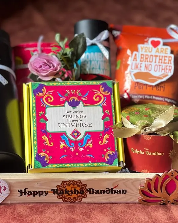 A personalized Rakhi hamper for a brother. This wooden tray includes a custom-engraved water bottle, snacks, and a quirky 'Siblings in every universe' box.