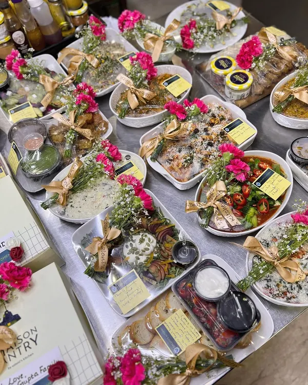 This is my pre-plated meal gifting service, a perfect way to send love through food. This spread shows a variety of dishes, from salads and appetizers to main courses, all beautifully garnished with fresh flowers and ribbons.