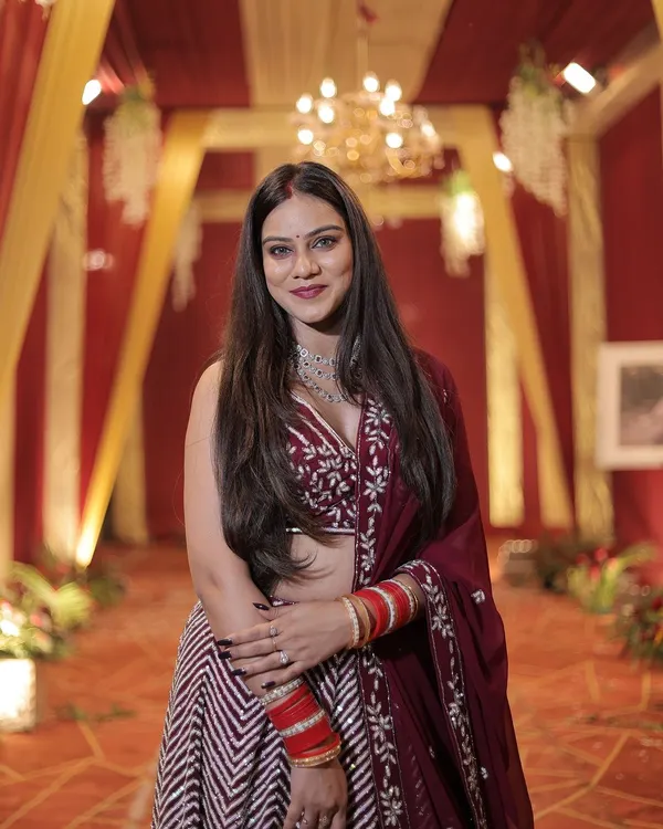 A happy client looking radiant in a maroon and white chevron pattern lehenga at a wedding reception. The outfit is paired with a modern diamond necklace.