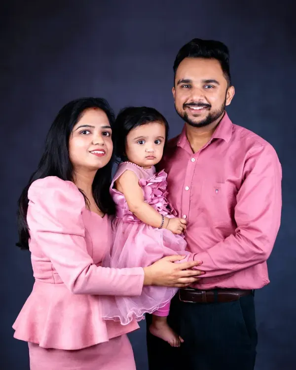 A beautiful family portrait against a dark backdrop. The coordinated pink outfits create a soft and loving feel in this classic standing pose.