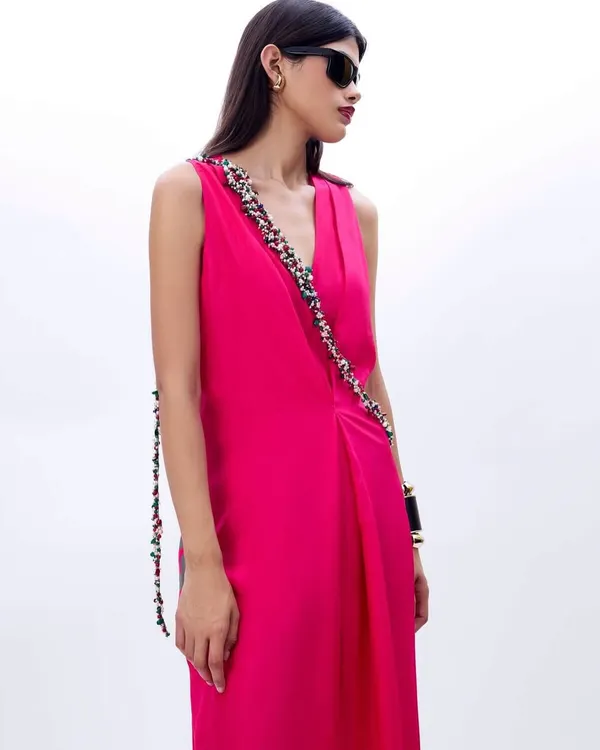 A silhouette that whispers elegance. A model in a vibrant fuchsia draped dress with a beautifully embellished strap detail.