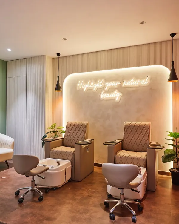 The pedicure station at HQ Smart Salons, designed for ultimate comfort. The combination of plush seating, warm ambient lighting from the neon sign, and gentle pendant lights creates a tranquil and luxurious atmosphere.