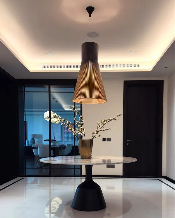 A minimalist foyer table designed to make a statement. The piece features a pure white marble top on a sculptural black pedestal base, creating a beautiful contrast on the polished marble floor.