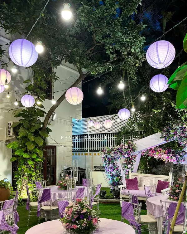 An enchanted evening under the stars. This garden party setup features a purple and lavender color scheme, with paper lanterns and string lights creating a magical canopy.