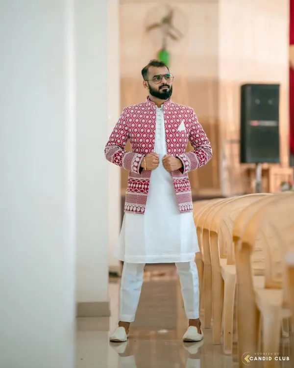 A client looking stylish in an open designer Jodhpuri set. The intricately embroidered red jacket is layered over a simple white kurta and pants, making it a perfect outfit for a Sangeet or wedding celebration.