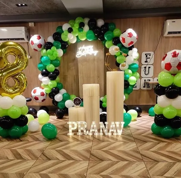 A fun football-themed birthday for an 8-year-old, featuring a green, black, and white balloon ring, football balloons, and personalized name blocks.