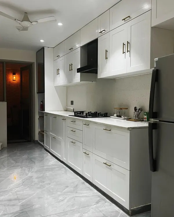 This parallel kitchen in Noida is designed for maximum efficiency. The all-white shaker-style cabinets create a bright and clean look, while the long countertops provide ample workspace.