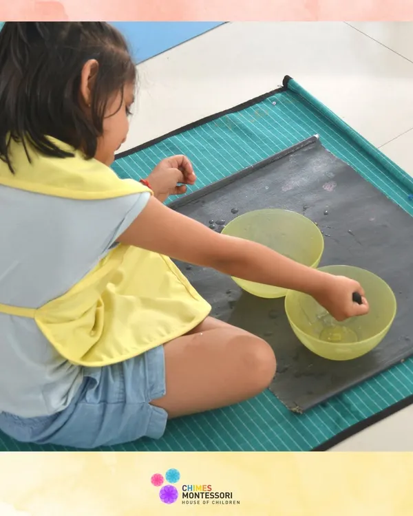 A child engages in a water-based practical life activity, learning control and precision while enjoying the sensory experience.