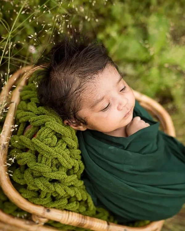 A newborn rests peacefully in a wicker basket, nestled in soft green wraps. This outdoor shot combines my love for nature with the delicate beauty of a new baby.