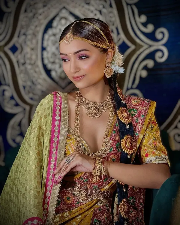 A beautiful South Indian bridal look, showcasing the traditional Kanjeevaram saree and temple jewelry. The makeup features warm tones and a classic braided hairstyle.