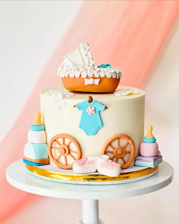 A beautiful baby shower cake with a vintage feel. The design includes a fondant baby carriage, booties, a onesie, and feeding bottles.