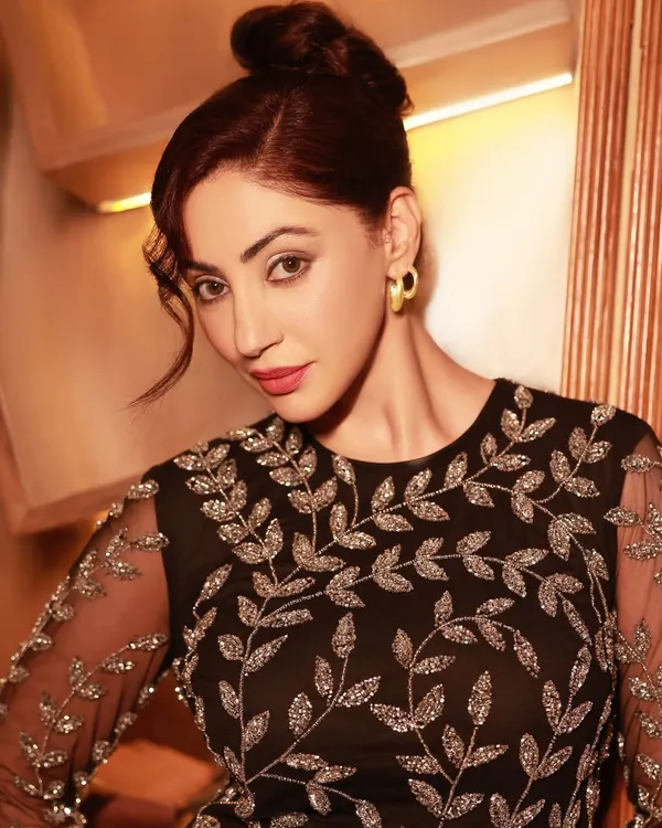 A portrait of actress Reyhna Pandit, capturing her elegance in an intricately embroidered black dress. The warm lighting and intimate setting create a timeless, sophisticated mood.