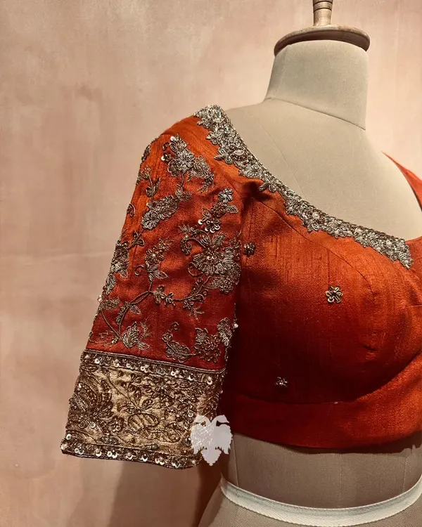 A close-up of a rust orange raw silk sleeve, adorned with delicate floral embroidery in zardosi, zari, and beads.