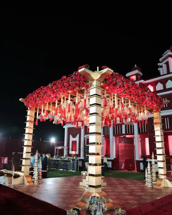 This wedding mandap was designed for a royal feel. Set against a palace-like structure, the mandap features a canopy of red roses and traditional hanging elements, creating a truly grand and opulent look.