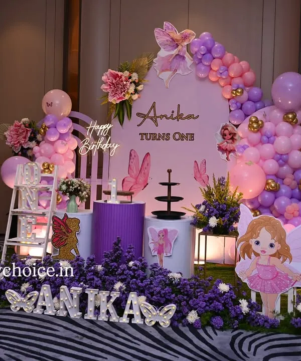 A stunning butterfly and fairy theme for a first birthday. This enchanting setup features a field of purple flowers, fairy and butterfly cutouts, a personalized backdrop, and beautiful pink and purple balloon arrangements.