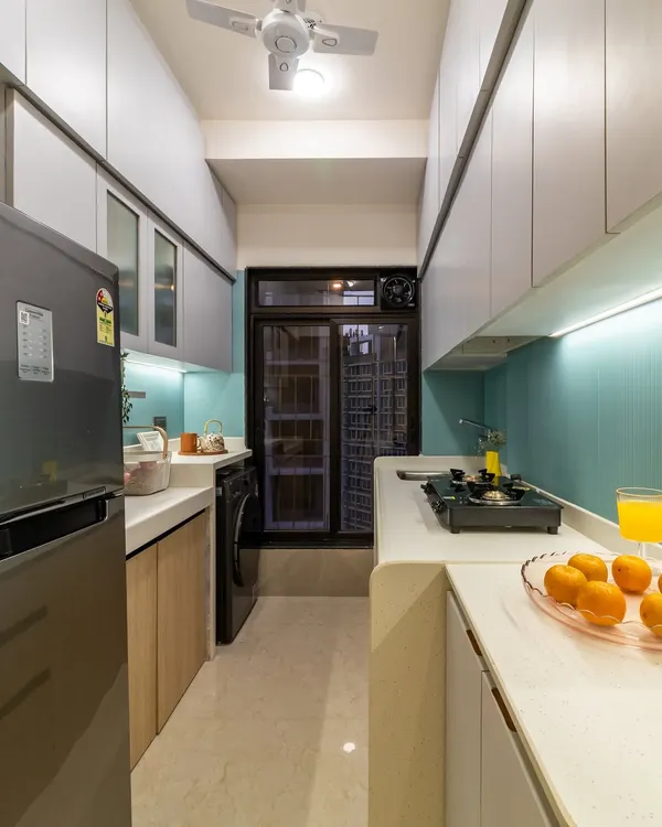 This compact kitchen renovation is a masterclass in space optimization. Pastel blue fluted tiles, light wood laminates, and handleless grey cabinets keep the narrow space feeling bright and airy.