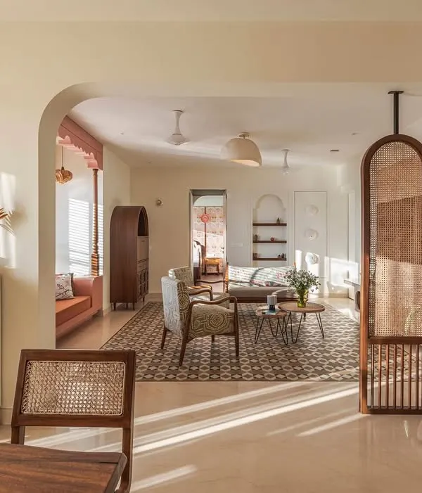 This living room is the heart of a home designed for tranquility. Sunlight streams in, highlighting the geometric floor tiles and the rich textures of the wooden furniture. A custom cane partition offers a glimpse into the dining area, creating an open yet intimate feel.