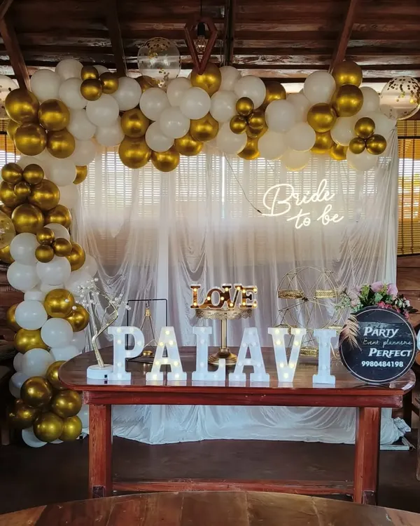 This 'Bride to be' decoration was set up within a rustic wooden gazebo, showing how I can adapt my designs to unique venues. The classic white and gold balloon arch, paired with a neon sign and the bride's name in marquee letters, beautifully complements the warm wood setting.