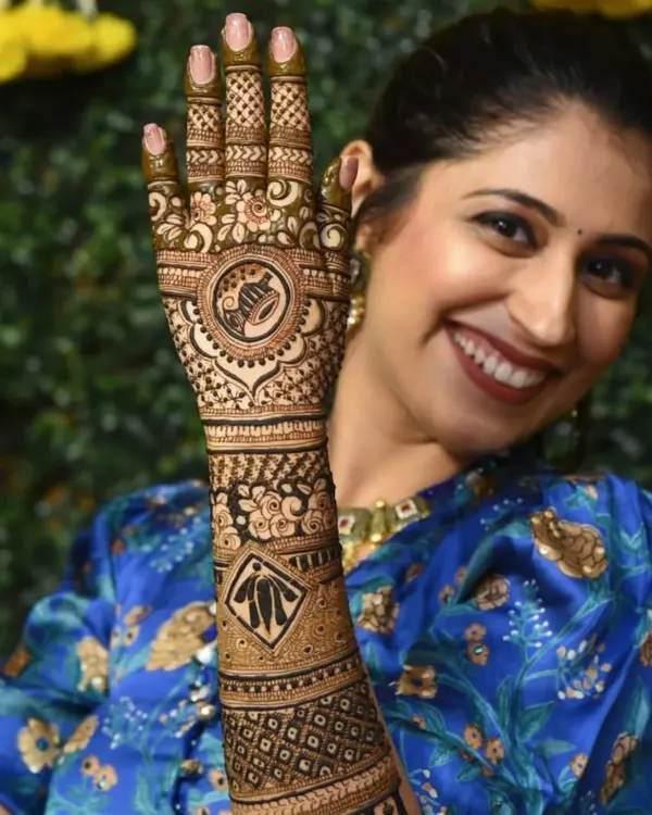 A happy bride showing off her personalized mehndi, which features a dhol and kalash, celebrating her culture.