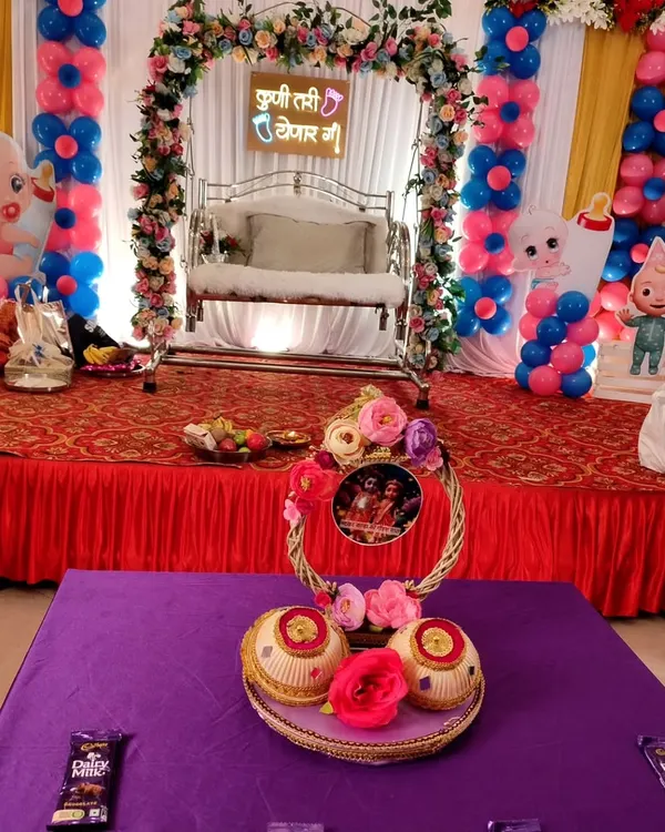 A beautiful stage setup for a traditional baby shower, complete with a decorated swing for the mom-to-be and festive pink and blue balloon columns.