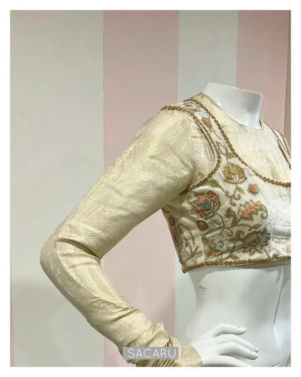 A unique double-layered saree blouse ensemble. It consists of an inner silk jacquard full-sleeve blouse, paired with an intricately embroidered velvet jacket.