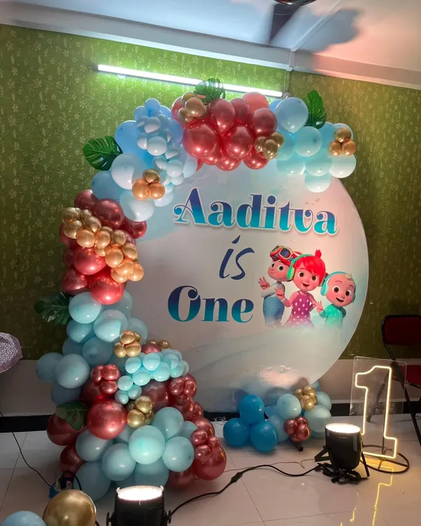 This Cocomelon theme for a first birthday is always a hit. The setup includes a circular backdrop with all the characters, a colorful balloon garland, and a light-up marquee number '1'.