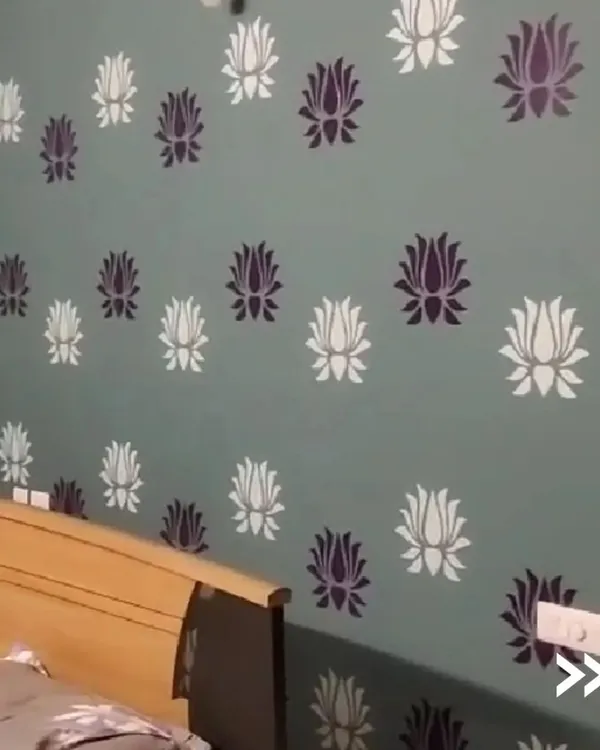 This bedroom accent wall features a beautiful two-tone lotus flower stencil. This technique is perfect for adding a touch of elegance and pattern to a room, creating a custom wallpaper effect with paint.