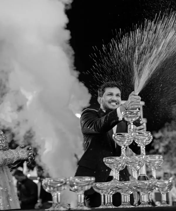 Kishan pops a bottle of champagne, creating a celebratory fountain. This black and white shot captures the energy and excitement of a wedding party, freezing the explosion of joy in time.