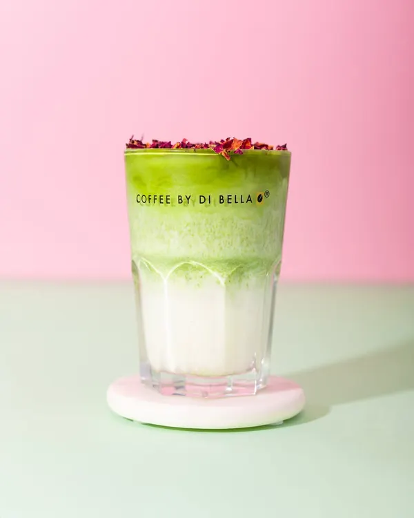 A vibrant Rose Matcha Latte from Coffee By Di Bella. The distinct layers of green and white, topped with rose petals, create a beautiful and Instagrammable image against a colorful background.