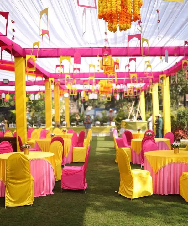 For this outdoor Haldi ceremony in Lonavala, we created a vibrant lounge atmosphere. The space is filled with bright yellow and pink seating, covered by a draped canopy that provides shade while adding to the festive color scheme.